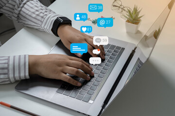 Person using a social media marketing concept on laptop with notification icons of like, chat, message and comment above laptop screen.