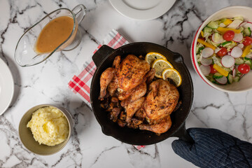 Cornish hens served in a cast iron pan on a white marble table with the side dishes