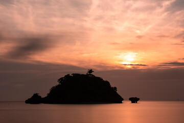 Naklejka na ściany i meble Sunset with beautiful shades of pink and orange and an island in silhouette resembling the shape of a whale on Sonai beach. Iriomote Island.