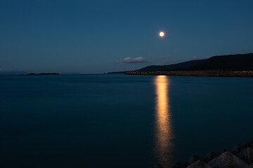 Fototapeta premium Beautiful twilight with the moon rising reflecting in the sea and mountain behind composing the beautiful view. Iriomote Island.