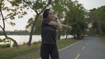 asian athlete woman in black sportswear stretching muscle warm up body for exercise and prevent injury at green lake park in sunset.