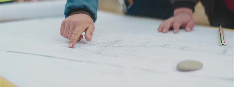 Engineers and Architects examining the blueprints and pointing with the fingers at it. Close-up shot.