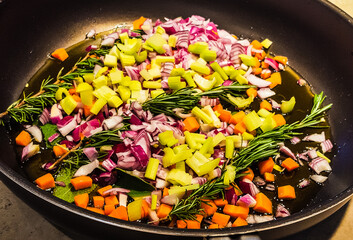 Fresh sprigs of rosemary along with diced carrots, celery and red onion cooking in a frying pan with olive oil