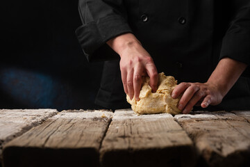 An experienced pro chef or baker in a professional kitchen prepares flour dough for pizza or pasta or bread. Italy, food, diet.Black background