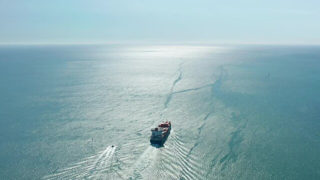 Aerial footage of two vessels floating across immense blue ocean. A cargo ship transports containers towards the horizon. High quality 4k footage