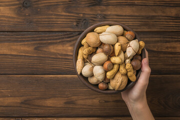 A woman's hand holds a bowl filled with nut mixture on a wooden background.