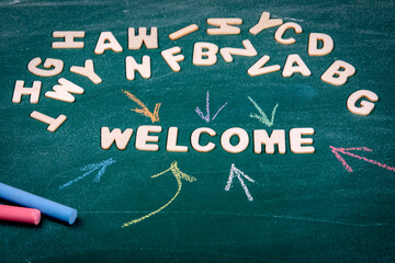 WELCOME. White letters of the wooden alphabet. Colored pieces of chalk