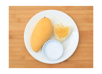 Golden mango and sticky rice served with coconut cream on white circle ceramic plate on bamboo board background. Tropical summer fruit in thailand. Top view