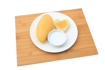 Golden mango and sticky rice served with coconut cream on white circle ceramic plate on bamboo board background. Tropical summer fruit in thailand