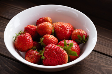 Natural ripe strawberries in a plain white bowl on a dark wooden table