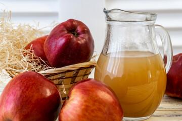 Red apples in a basket and apple juice in a jug on a wooden table