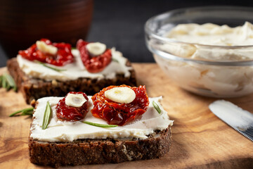 Homemade multigrain bread sandwiches with cream cheese and sun-dried tomatoes on a wooden platter, close-up. Healthy eating concept