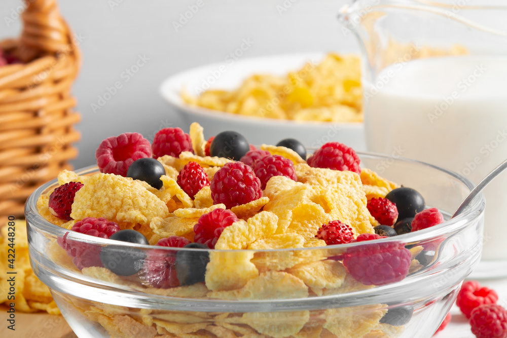 Wall mural Glass bowl with cereal flakes and berries and milk on the table, close-up. Healthy summer breakfast