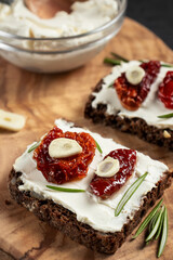 Homemade multigrain bread sandwiches with cream cheese and sun-dried tomatoes on a wooden platter. Healthy eating concept. Vertical image