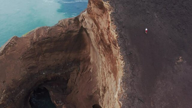 Done shot of male tourist exploring nature of Capelinhos Volcano, Faial Island, Azores, Portugal, Europe. Zoom out view of man hiking on top pf rock at atlantic ocean. 4k footage