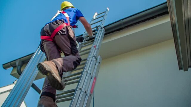 Secured professional male worker climbs up ladder on roof on sunny day