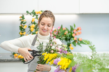 Smiling woman wearing apron arranging a bouquet of beautiful colorful flowers inside her floral shop