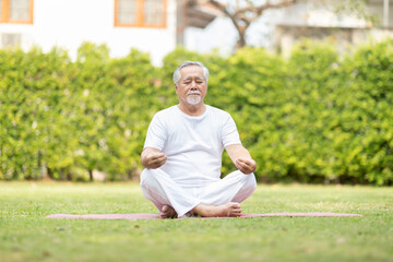 Naklejka premium Calm of Healthy Asian Elderly man with white hairs doing yoga lotus pose for meditation on green grass at park,Wellness Senior Recreation with yoga concept