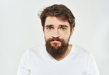 Obraz premium Emotional guy in a white T-shirt on a light background cropped view of a thick beard of a brunette
