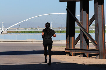 Jogger runs past structural steel beams along a lakefront path, with a modern pedestrian bridge in...