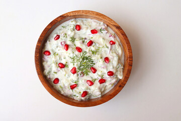 Indian Fresh sauce or condiment called Raita. Yogurt mixed with grated cucumber, onions, pomegranate, and spices. Garnished with fresh coriander. Copy space.