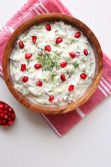 Indian Fresh sauce or condiment called Raita. Yogurt mixed with grated cucumber, onions, pomegranate, and spices. Garnished with fresh coriander. Copy space.