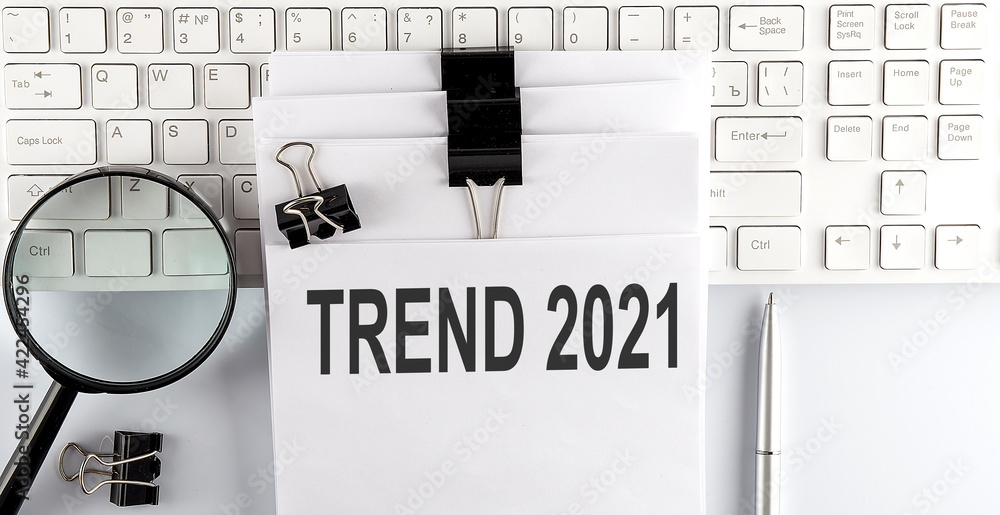 Poster words trend 2021 written on papers on a computer keyboard with magnifier and pen