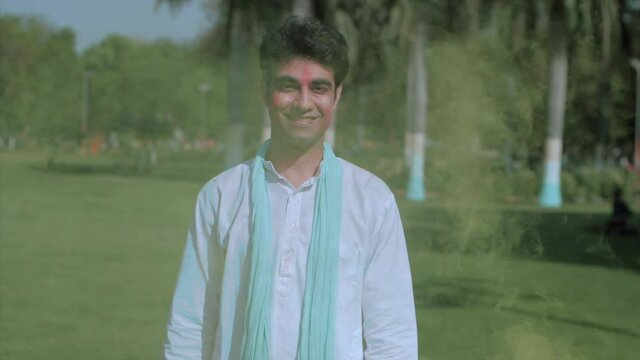 Handsome Indian guy standing among the smoke of colorful Gulal in the air. Medium shot of a smiling man wearing traditional clothes enjoying Holi festival standing outdoors