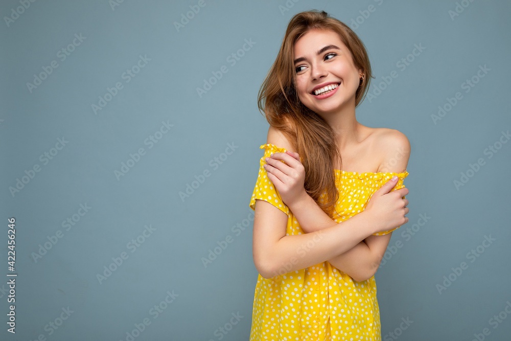 Wall mural Photo shot of pretty joyful smiling young female person wearing casual trendy outfit standing isolated on colourful background with copy space looking to the side and having fun