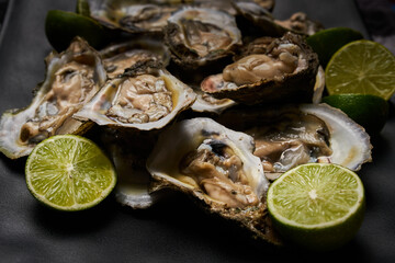 Ostras abiertas, preparadas con limón y sal, puestas sobre un plato cuadrado negro en una tabla de...