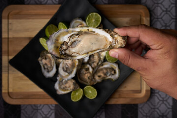 Ostras abiertas, preparadas con limón y sal, puestas sobre un plato cuadrado negro en una tabla de...