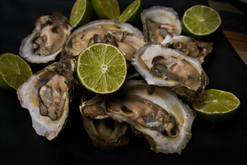 Ostras abiertas, preparadas con limón y sal, puestas sobre un plato cuadrado negro en una tabla de madera