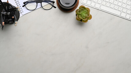 Top view of workplace with keyboard, coffee cup, glasses and  notebook on marble background. Copy space for products display montage.