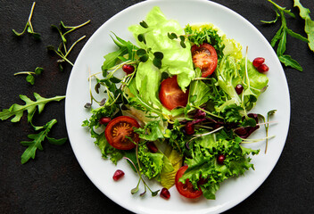 Fresh green mixed  salad bowl with tomatoes and microgreens  on black concrete background. Healthy food, top view.