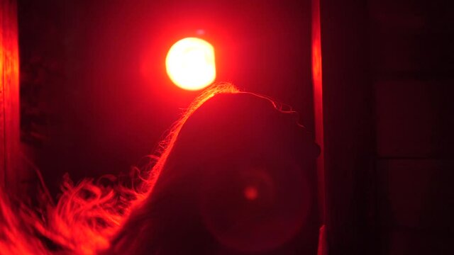 A beautiful girl waves her long blond hair. Profile of a beautiful girl in a dark room