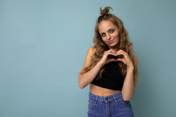 Fototapeta premium Photo of young positive happy smiling beautiful woman with sincere emotions wearing stylish clothes isolated over background with copy space and showing heart gesture