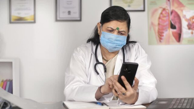 Doctor using a mobile phone to inform her patient about medical test results. A female physician wearing a white uniform using a touchscreen device in her clinic - remote consultation / telemedicin...