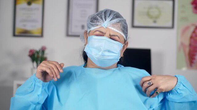 Senior medical practitioner feeling pain and discomfort in her neck and shoulder. An exhausted healthcare worker in personal protective wear (PPE Kit) after long working hours in the medical facility