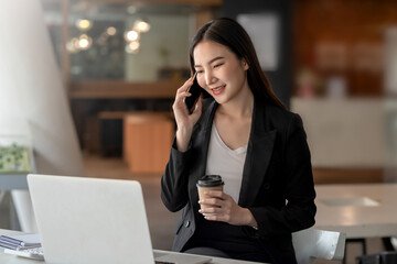 Asian businesswoman talking on the phone holding a coffee mug in the office.