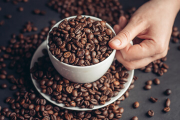 coffee beans In a saucer and in a cup of coffee on a gray background female hand macro photography