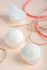 Coconut truffles or homemade organic energy balls with a filling of sweetened shredded coconut, condensed milk and curd cheese on pink background with red ribbon and packing twine. Vertical image