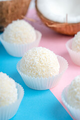 Coconut truffles or homemade organic energy balls with a filling of sweetened shredded coconut, condensed milk and curd cheese laying on trendy colorful pink and blue background. Vertical image