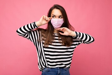 Shot of young attractive woman wearing mediacal face mask isolated over background wall. Protection against COVID-19