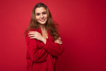 Portrait of young attractive caucasian hipster woman in trendy casual clothes. Sexy carefree female person posing isolated near red wall in studio. Positive model with natural makeup. Empty space