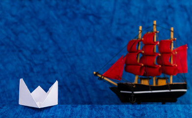 A small white paper boat and a toy ship behind representing professionalism concept.