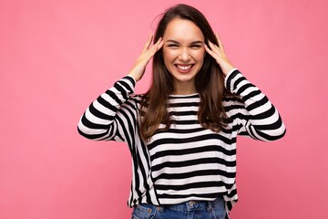 Photo of young positive happy smiling beautiful brunette woman with sincere emotions wearing casual striped pullover isolated on pink background with copy space