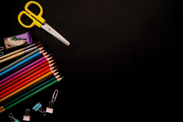 Colored pencils,paper clips, and clips are arranged in a row on a black background.