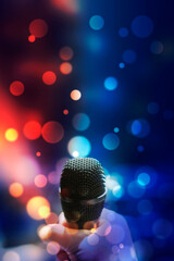 Hand holding a microphone against colourful background.