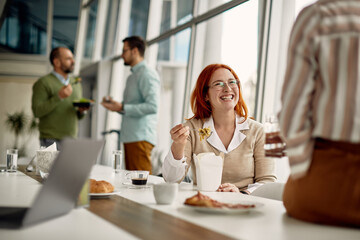 Cheerful businesswoman having fun on lunch break while communicating with co-worker at the office.