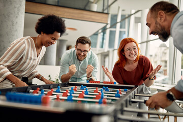 Group of happy business co-workers playing table football on break in the office.